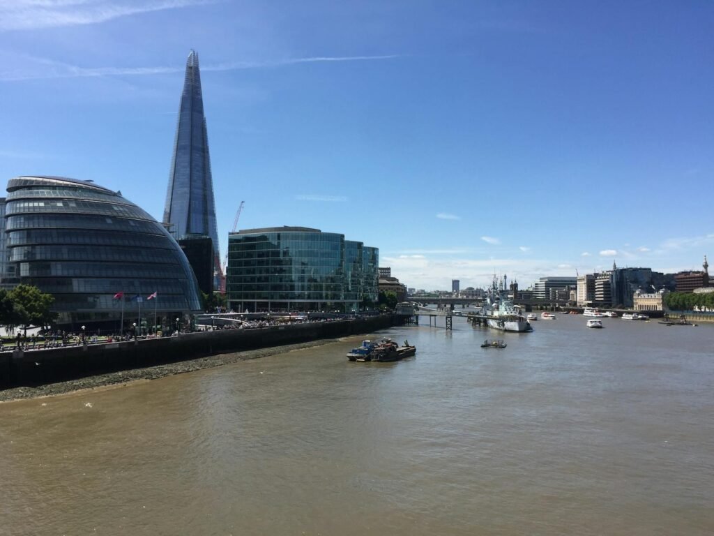 Panoramic view of The Shard and City Hall along the River Thames in London, showcasing urban architecture and river activity.